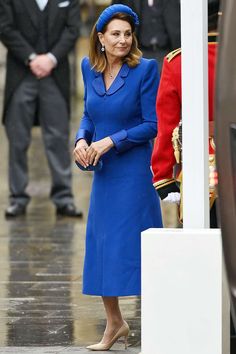 the queen is wearing a bright blue dress and matching hat as she stands in front of an official car