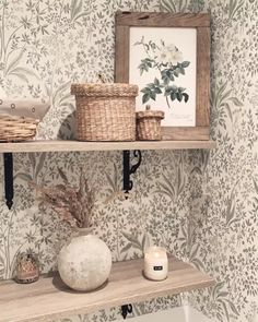 two shelves with baskets and candles on them in front of a wallpapered wall