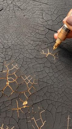 a person is writing on the cracked surface with a pen and ink bottle in their hand