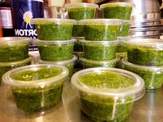 several plastic containers filled with green food sitting on top of a metal counter next to a canister