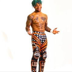 a man with dreadlocks and tattoos standing in front of a white background wearing patterned pants