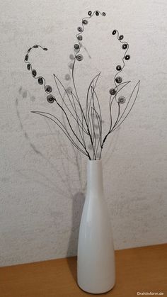 a white vase with black flowers in it on a wooden table next to a wall