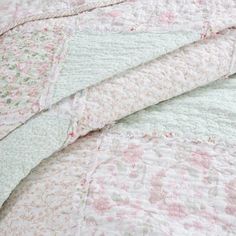 an unmade bed with pink, green and white quilted bedspread on it