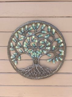 a metal tree with green leaves is mounted on the side of a building, and it looks like an art work