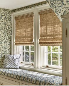 a window seat in front of two windows with roman shades