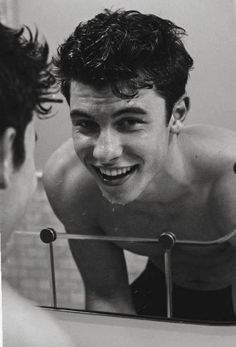 black and white photograph of a man smiling in front of a mirror with his reflection