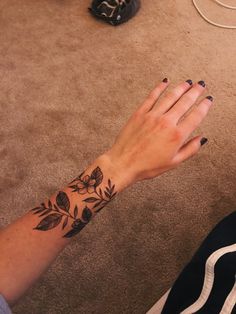 a woman's hand with a flower tattoo on her left wrist and black nail polish