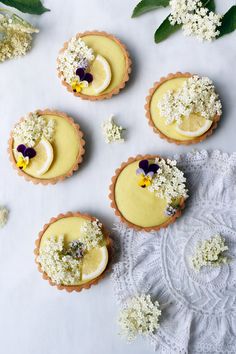 several small pies with flowers and leaves on top of a white table cloth next to each other