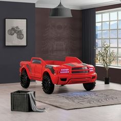 a red truck is parked in a room with a large window and rug on the floor