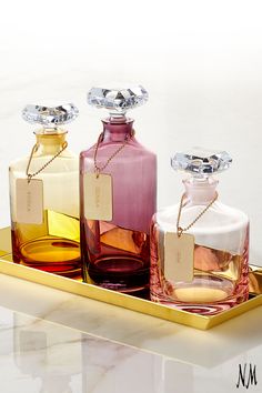 three small bottles with tags on them sitting on a gold tray in front of a marble wall