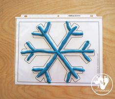 a snowflake made out of blue plastic on top of a wooden table next to a piece of paper