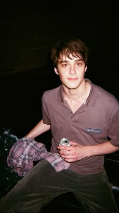 a young man sitting on the ground with a can in his hand and looking at the camera