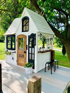 a small white house sitting on top of a wooden deck next to a large tree