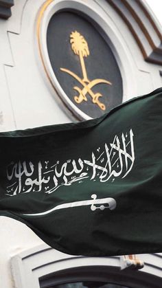 a flag flying in front of a clock tower with arabic writing on it's side