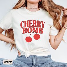 This retro/vintage style tee features the saying "Cherry Bomb" with a cherry graphic on the front of the shirt. This t-shirt is the perfect minimalist and stylish piece to add to your wardrobe. This top is trendy yet timeless making it perfect for any occasion, or as a gift.  💛 SIZING 💛 - This t-shirt comes in unisex sizing. - If you're looking for an oversized look, we recommend sizing up one to two sizes. - Our size chart is listed in the pictures above, please use this chart for the most ac Trendy Crew Neck T-shirt With Cherry Print, Retro Slogan T-shirt For Spring, Retro Cherry Print T-shirt For Summer, Retro Slogan Tops, Retro Slogan Tops For Spring, Retro Letter Print T-shirt For Spring, Vintage Cotton T-shirt With Funny Text, Y2k T-shirt With Cherry Print, Y2k T-shirt With Funny Text For Spring