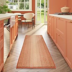 an orange kitchen with pink walls and wooden flooring, along with white chairs in the dining area