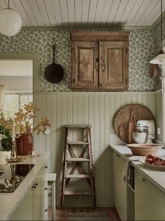 an old fashioned kitchen with green wallpaper and white counter tops, wooden cabinetry