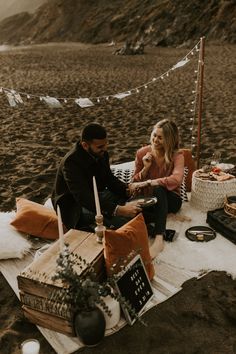 a man and woman sitting on the beach next to each other with food in front of them