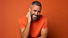 a man smiling and holding his hand to his ear with an orange wall in the background