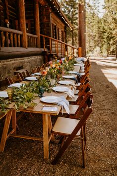 a long table set up with plates and place settings for an outdoor dinner in the woods