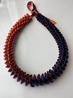 an orange and blue necklace is hanging on a white surface with a ribbon around it