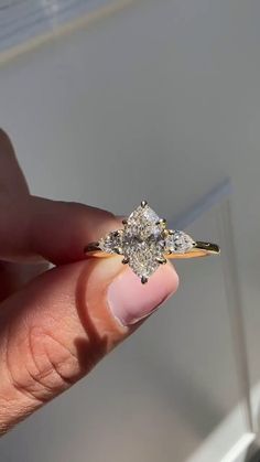 a woman's hand holding an engagement ring with three diamonds on it, in front of a window