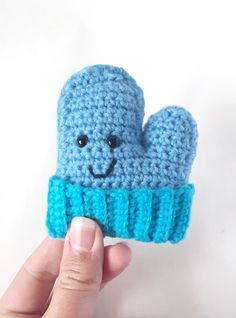 a crocheted blue mitten with a smiling face is held up to the camera