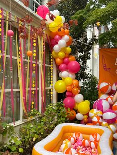 an inflatable pool surrounded by balloons, streamers and streamers on the side of a building