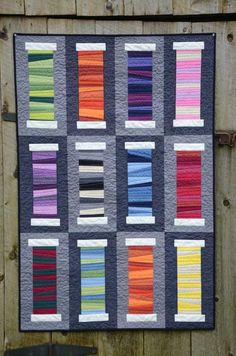 a quilted wall hanging on the side of a wooden fence with multiple colors of yarn