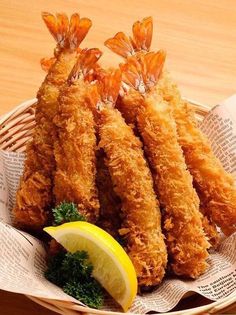 some fried food in a basket with lemon wedges and parsley on the side