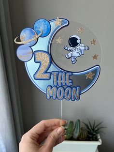 a hand holding up a cake topper with an image of the moon on it