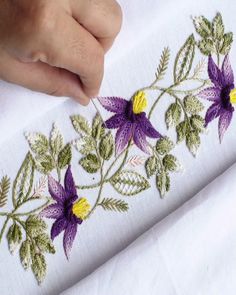 a person is stitching flowers on a white piece of cloth with green and yellow leaves