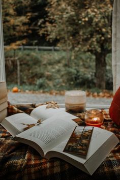 an open book sitting on top of a bed next to a candle and some books