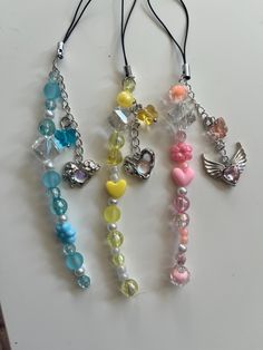 three necklaces with charms attached to them on a table top, one is multicolored and the other has an angel charm