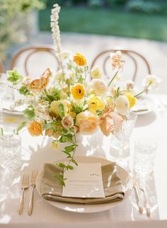 the table is set with white and yellow flowers, silverware, and napkins