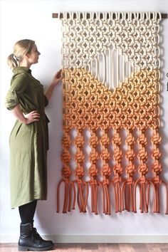 a woman standing in front of a wall hanging with orange and white crochet