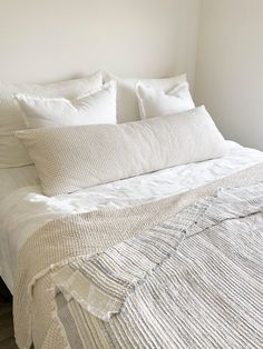 a bed with white linens and pillows in a small room, all made up