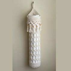 a white crocheted tube hanging on a wall with tassels and beads