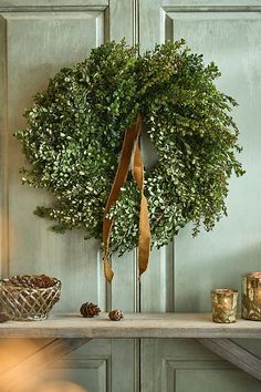 a wreath is hanging on the wall above a table with candles and pine cones in front of it