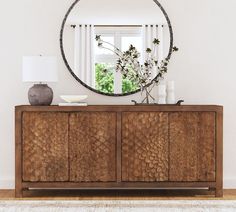 a wooden cabinet with a round mirror above it and vases on the sideboard