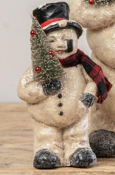 two snowmen with hats and scarves are standing next to each other in front of a christmas tree