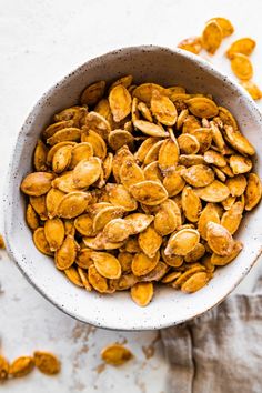 a white bowl filled with pumpkin seeds on top of a table next to a napkin