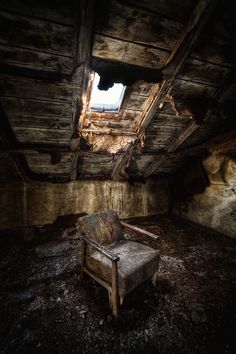 an old chair sitting in the middle of a room filled with dirt and wood planks