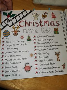 a christmas movie list on a wooden table with a hand holding a pen and pencil