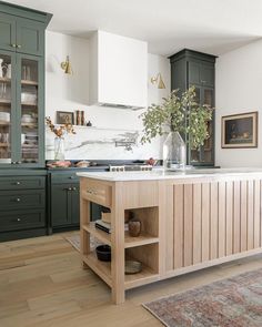 a kitchen with green cabinets and an island in front of the countertop, along with a rug on the floor