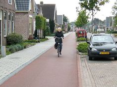 a woman riding a bike down a street next to parked cars and houses on both sides