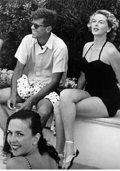 three people sitting next to each other on the edge of a swimming pool in bathing suits