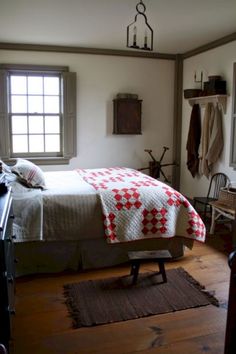 a bed sitting in a bedroom next to a window with a red and white quilt on it