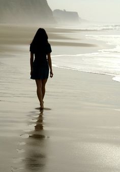 a woman walking along the beach towards the ocean