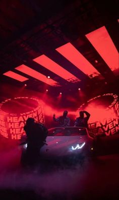 two people standing on top of a car in front of red light emitting from the roof